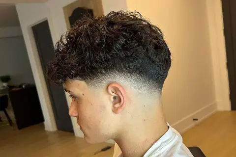 Joven con cabello rizado oscuro y un corte moderno con **low fade** impecable, creando un degradado suave y estilizado en los laterales.