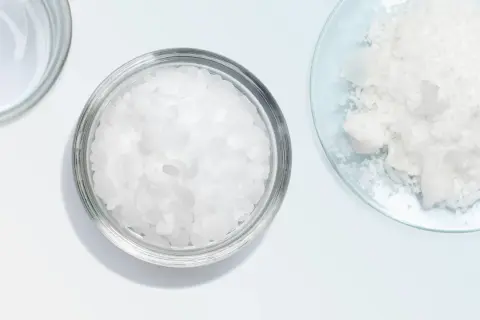 Botes con escamas blancas, como cetearyl alcohol, y un polvo blanco en un plato de vidrio.