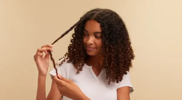 Chica con cabello rizado oscuro, aplicando el método curly a un mechón.