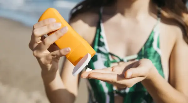 Mujer aplica protector solar en su mano. Aprende cómo quitar manchas de crema solar de la ropa y piel.
