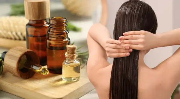 Aceite de romero para el pelo, aplicado en cabello largo y oscuro. Botellas de aceite y ramitas de romero al lado.