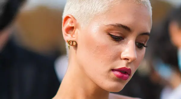 Mujer con atrevidos rapado cortes de pelo corto, luce un maquillaje audaz y pendientes dorados.