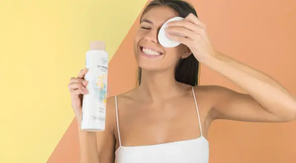 Mujer sonriente con agua micelar y disco desmaquillante, parte de su rutina limpieza facial.