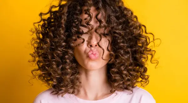 Chica con rizos perfectos, besando al aire. Su cabello luce espectacular gracias al método curlt.