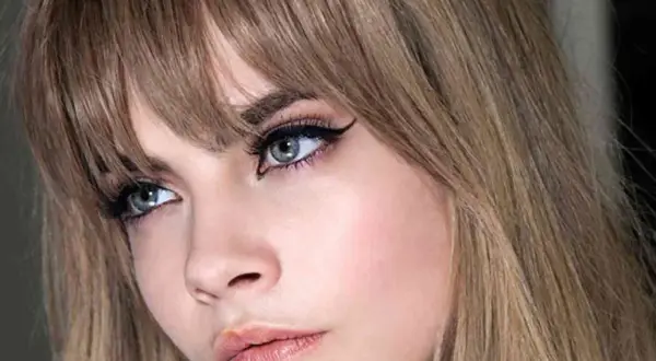 Primer plano de una mujer con flequillo recto y ojos maquillados con delineado cat eye. Explora los tipos de flequillo.