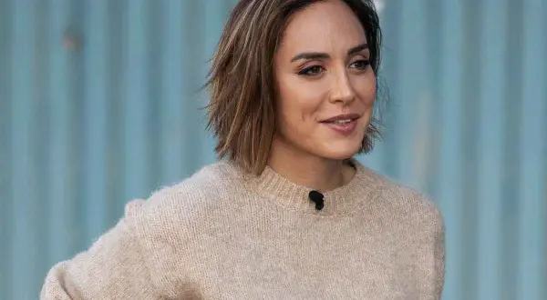 Mujer con un moderno corte bob con flequillo, luciendo un suéter beige y una sonrisa amable.