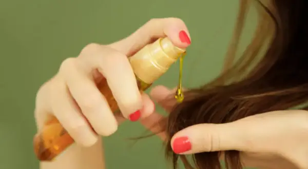 Mano aplica aceite capilar, un producto común en cosmética por sus siliconas, para dar brillo y suavidad al cabello.