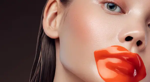 Labios rojos y brillantes cubren la boca de una mujer. Quizás para evitar que se diga que exfoliar los labios es malo.