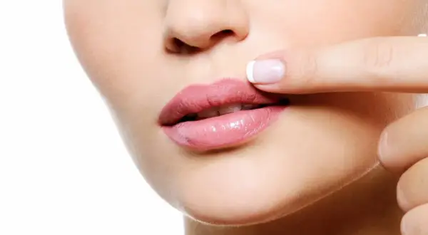 Dedo tocando labios rosados, notando pequeños granitos en los labios.