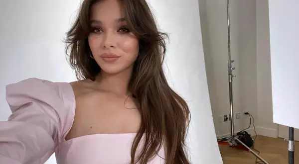 Mujer con cabello largo y castaño, peinado con un corte mariposa, luce un vestido rosa con mangas abullonadas.