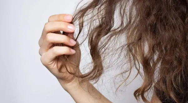 Mano sujetando mechones de cabello castaño, mostrando la necesidad de una repolarización capilar para revitalizarlo.