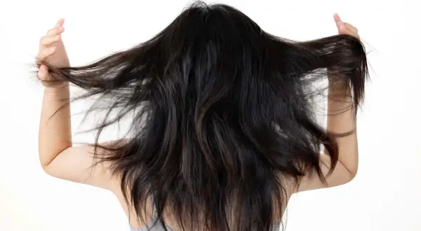 Mujer con cabello oscuro y largo, moviéndolo con las manos. Busca un alisado natural para domar su melena.