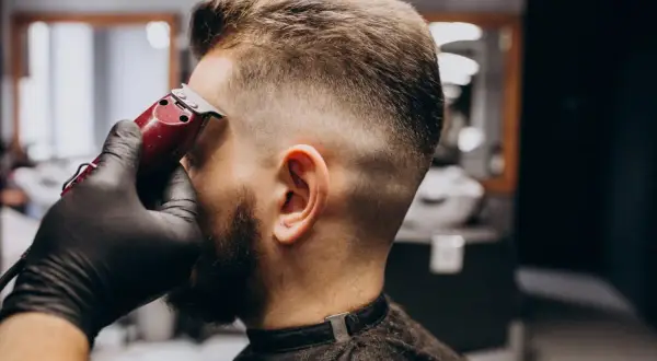 Barbero dando forma a un corte buzz cut fade con una máquina.