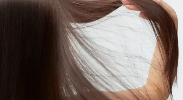 Cabello castaño oscuro y sedoso, con una mano acariciando las puntas. Descubre cómo cuidar el pelo fino para lograr este aspecto.