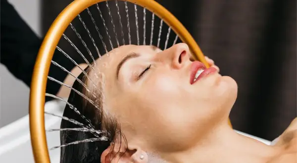 Mujer disfrutando de un relajante spa para cabello con agua cayendo sobre su rostro.