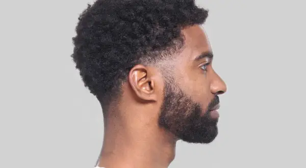 Perfil de hombre con cabello rizado y barba, luciendo un moderno corte taper fade.