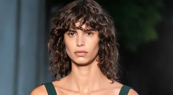Modelo con un moderno corte de pelo rizado a capas, con mechones que enmarcan su rostro.