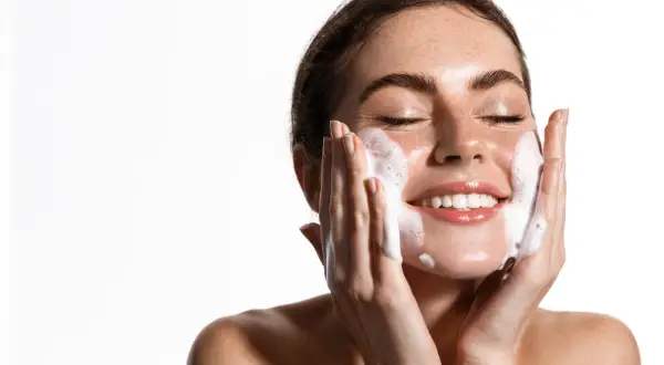 Una mujer sonríe mientras se realiza una limpieza facial noche con espuma.