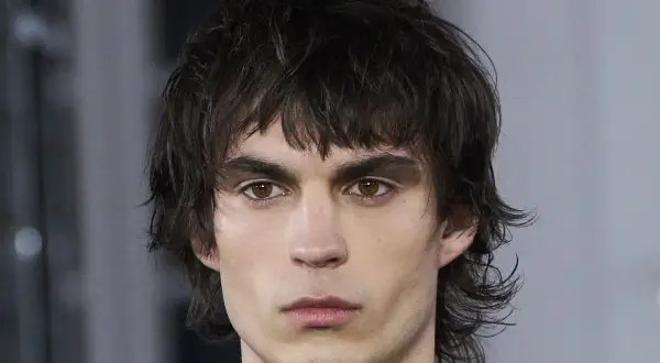 Hombre joven con un moderno mullet corto, cabello oscuro y despeinado, mirada intensa.