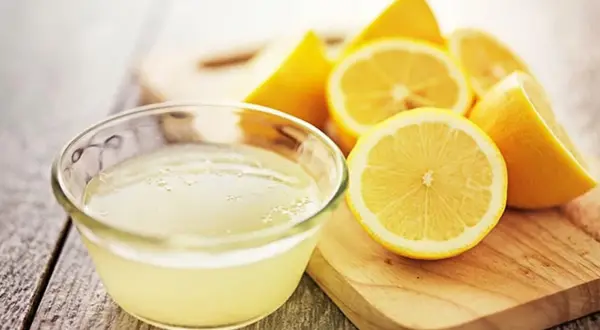 Un tazón de jugo de limón fresco y limones cortados, ideales como remedios caseros para el pelo graso.
