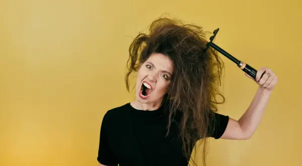 Mujer frustrada con su pelo seco y encrespado, intentando peinarlo con un cepillo.