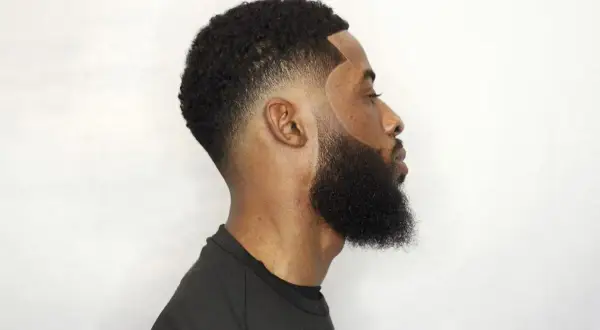 Hombre con un corte de pelo con tuper fade y barba cuidada, perfilado impecable.