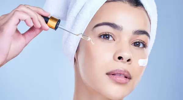 Una mujer con toalla en la cabeza aplica un suero con gotero, ideal para usar niacinamida y retinol juntos.