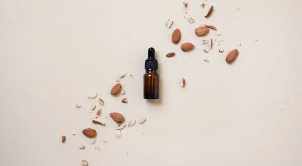Frasco de aceite de almendras para el pelo rodeado de almendras enteras y trozos.