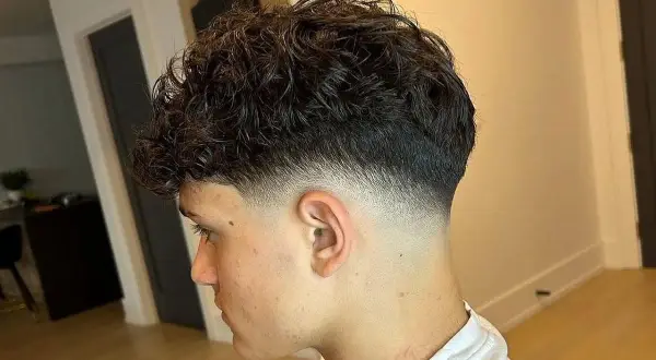 Joven con cabello rizado oscuro y un corte moderno con **low fade** impecable, creando un degradado suave y estilizado en los laterales.