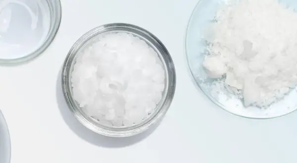 Botes con escamas blancas, como cetearyl alcohol, y un polvo blanco en un plato de vidrio.