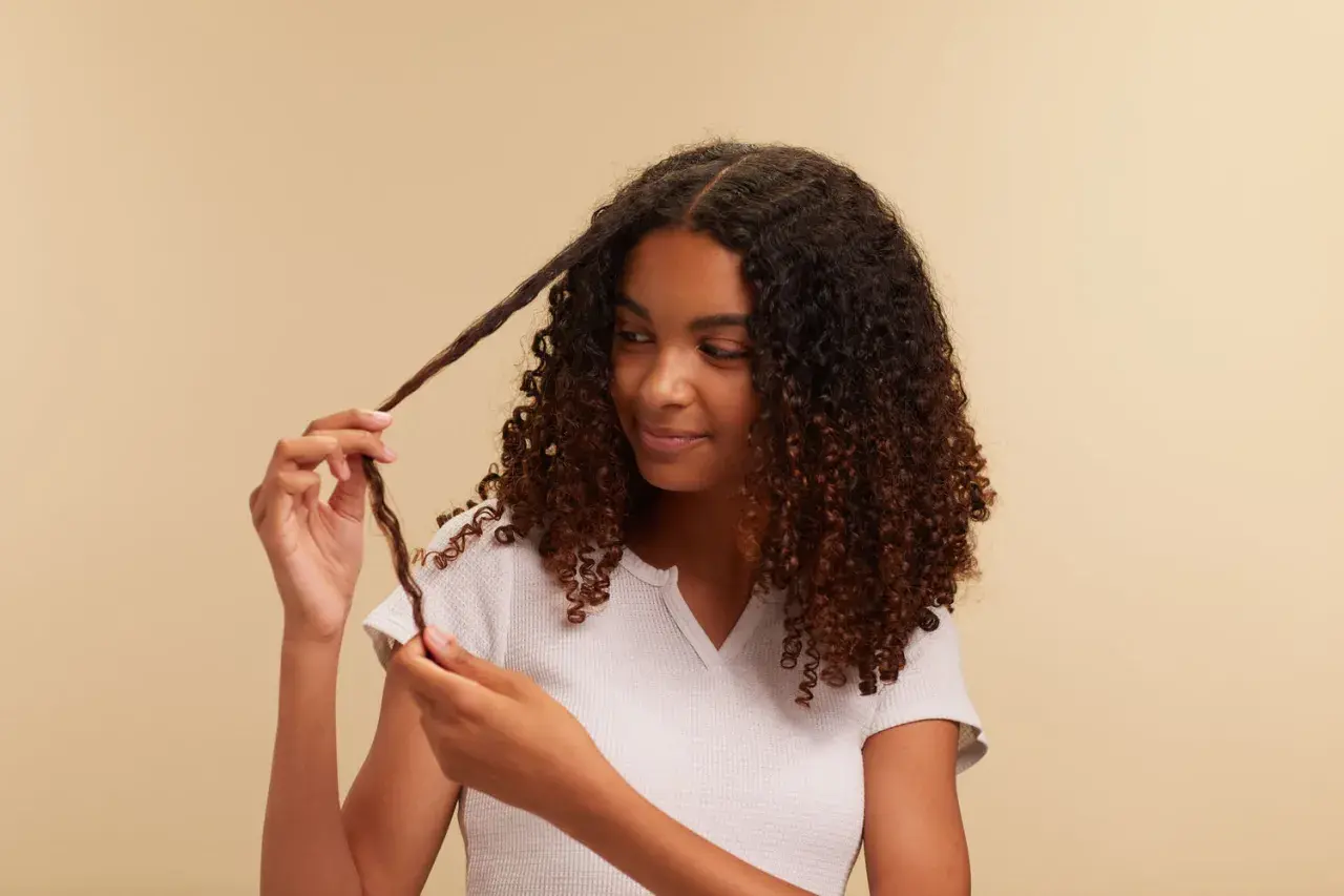 Chica con cabello rizado oscuro, aplicando el método curly a un mechón.
