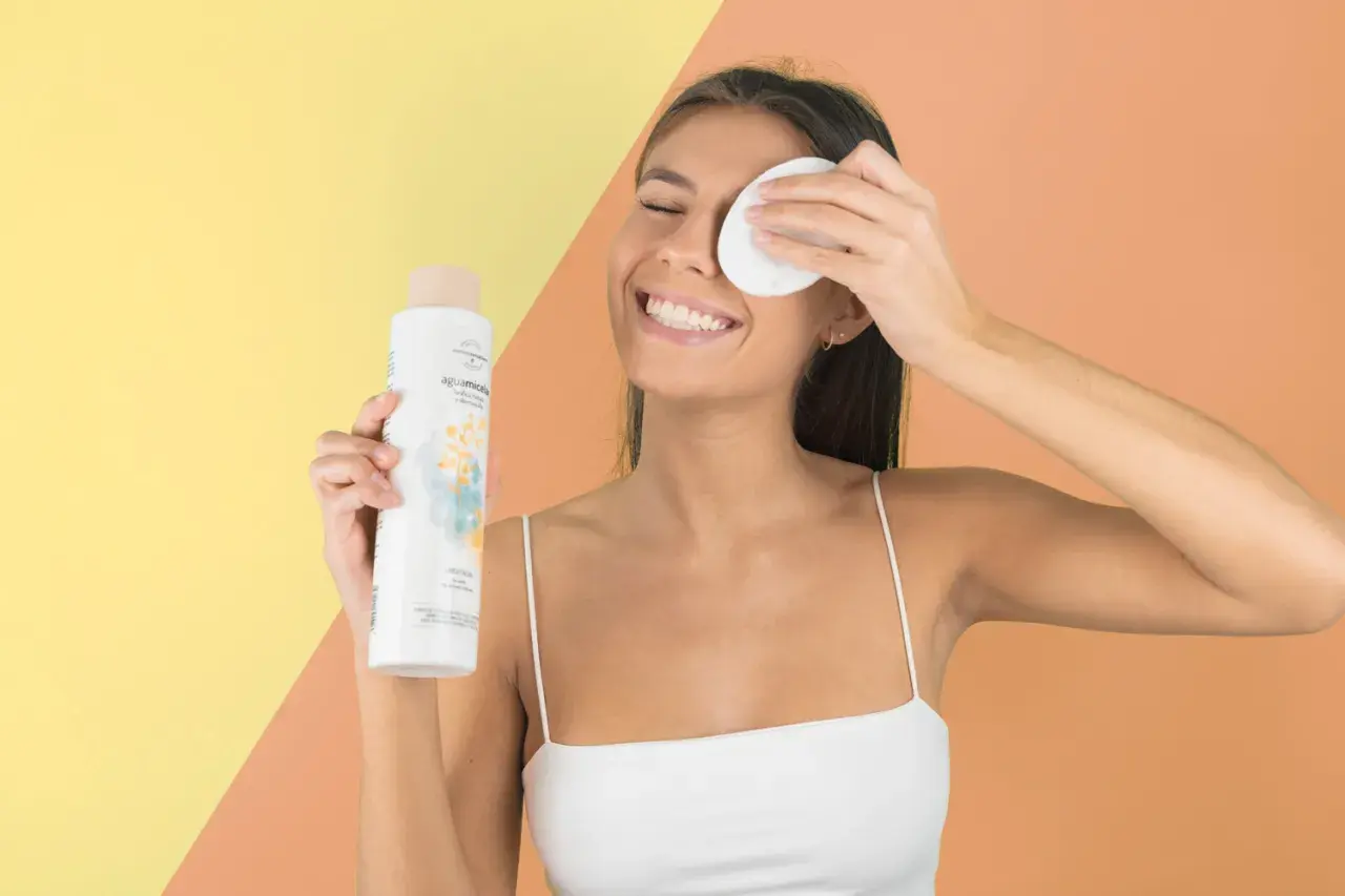 Mujer sonriente con agua micelar y disco desmaquillante, parte de su rutina limpieza facial.
