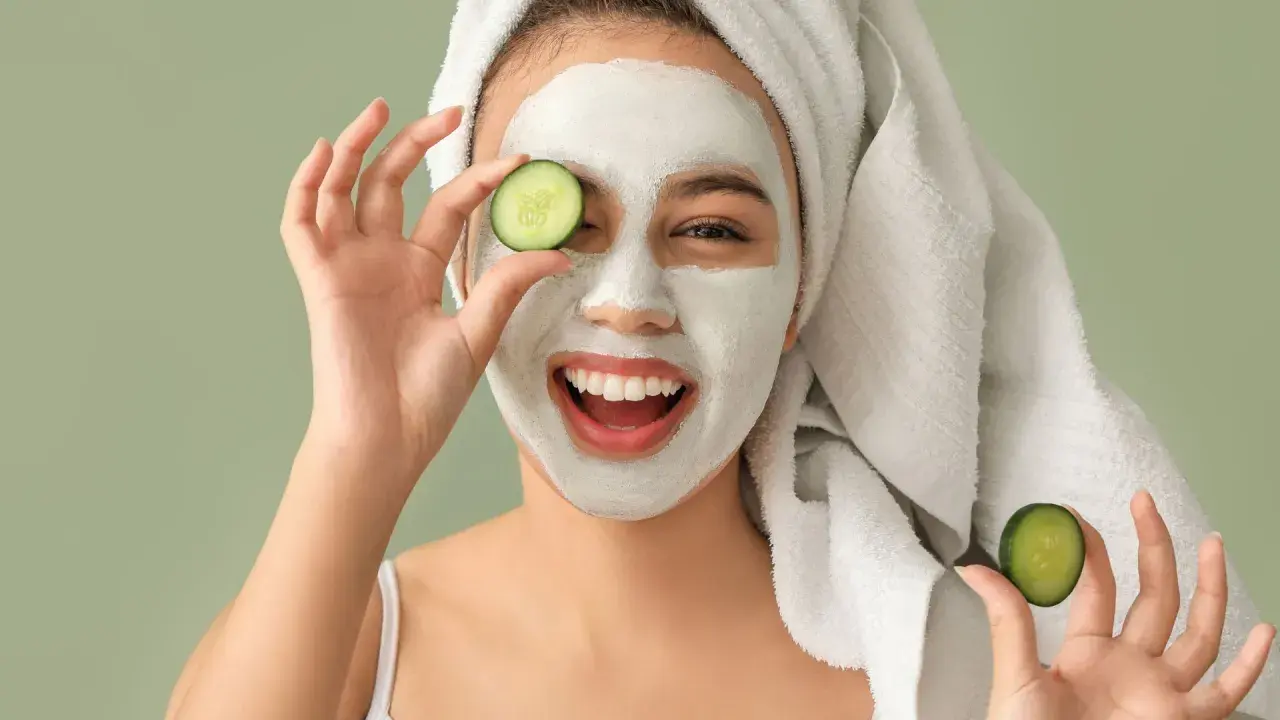 Mujer sonriente con mascarilla facial y rodajas de pepino, disfrutando de tratamientos faciales naturales.
