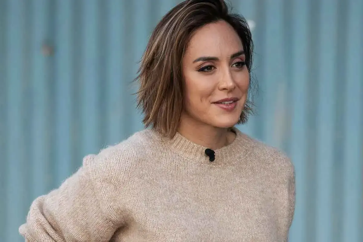 Mujer con un moderno corte bob con flequillo, luciendo un suéter beige y una sonrisa amable.