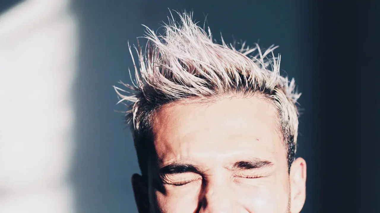 Hombre con pelo rubio despeinado y ojos cerrados. Consejos sobre como hidratar el pelo hombre para un look fresco.
