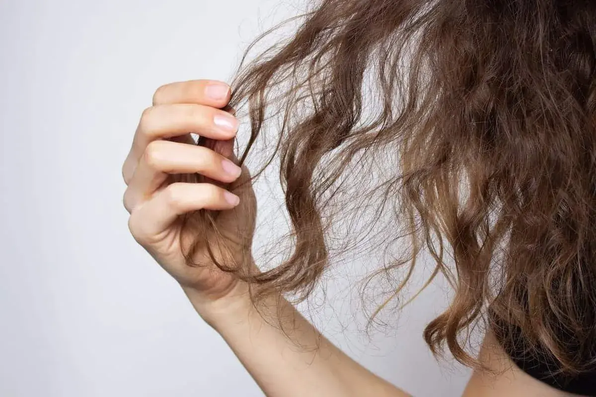 Mano sujetando mechones de cabello castaño, mostrando la necesidad de una repolarización capilar para revitalizarlo.
