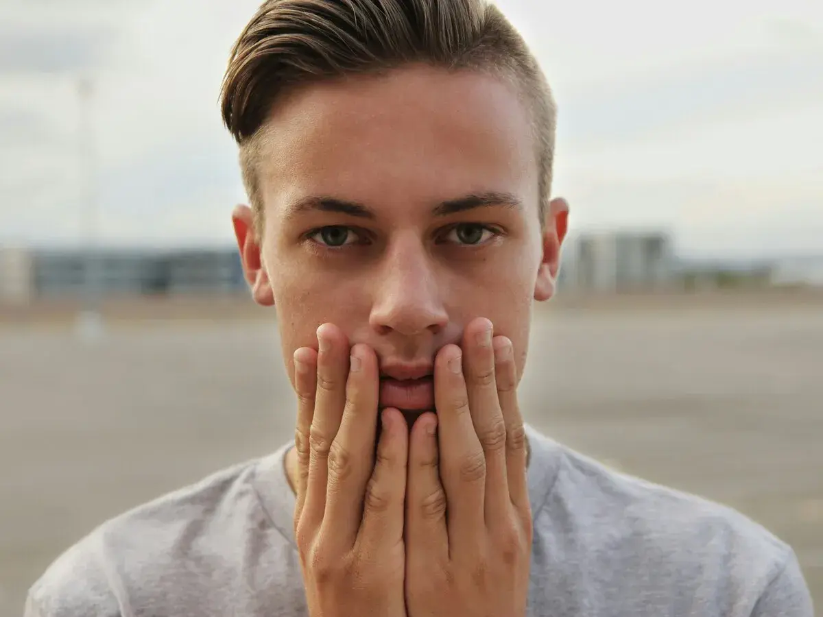 Primer plano de un joven con las manos en la cara, su peinado degradado resalta sus ojos verdes.