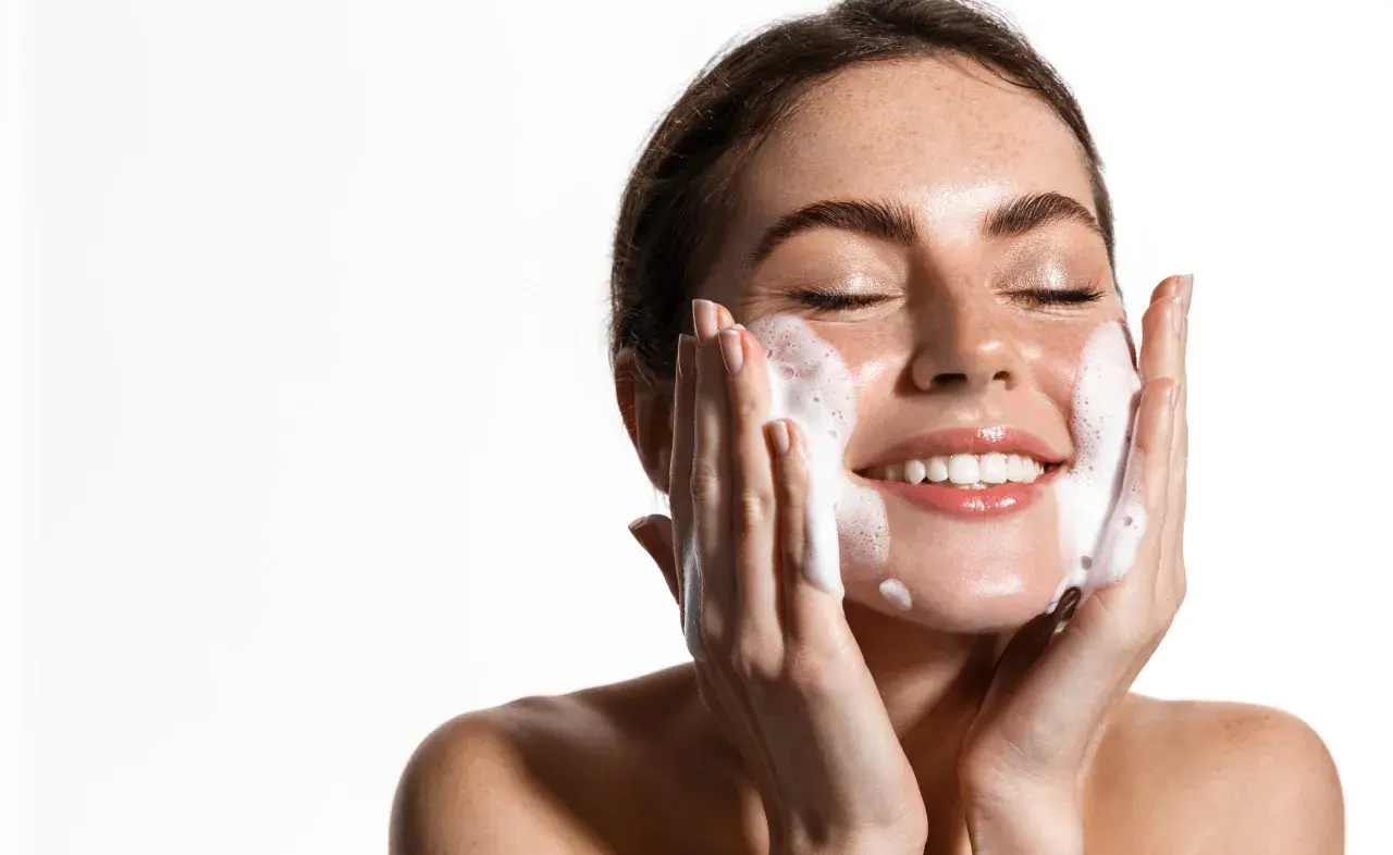 Una mujer sonríe mientras se realiza una limpieza facial noche con espuma.