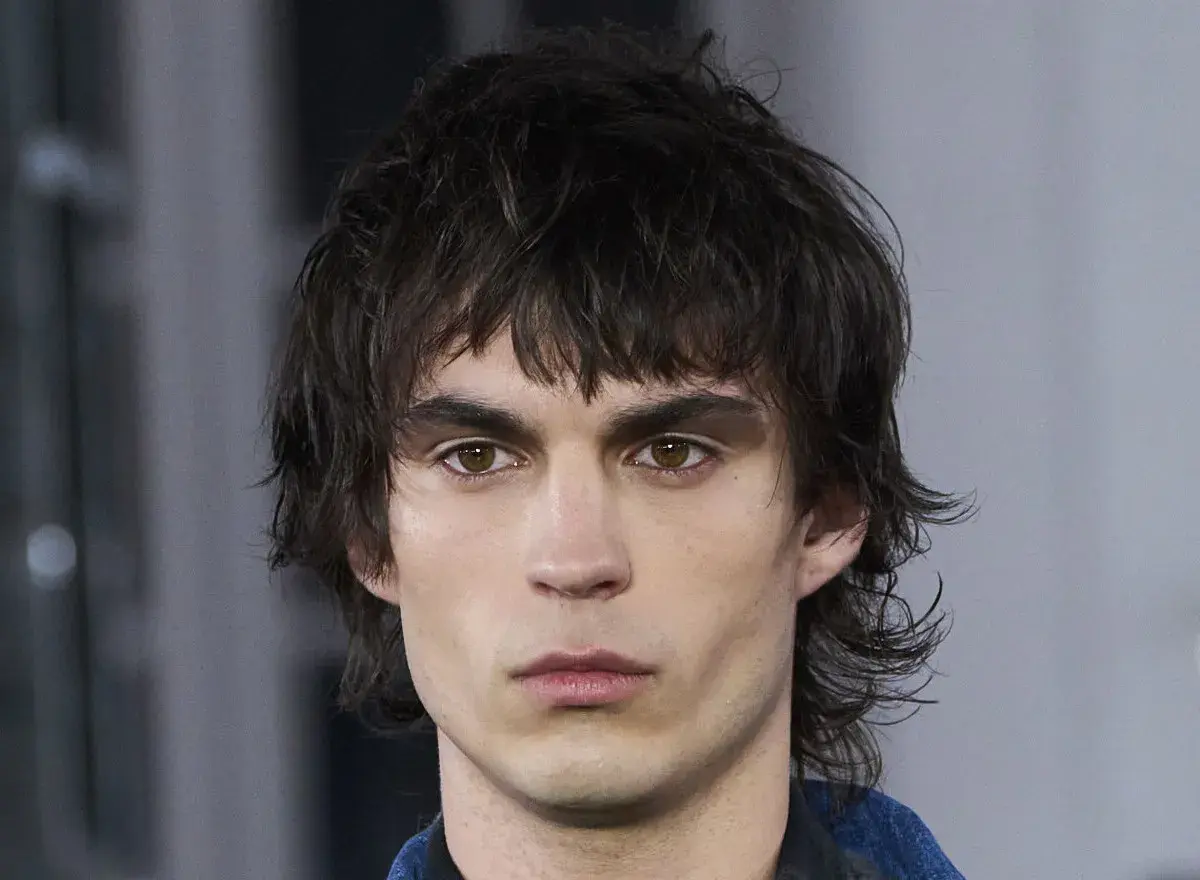 Hombre joven con un moderno mullet corto, cabello oscuro y despeinado, mirada intensa.