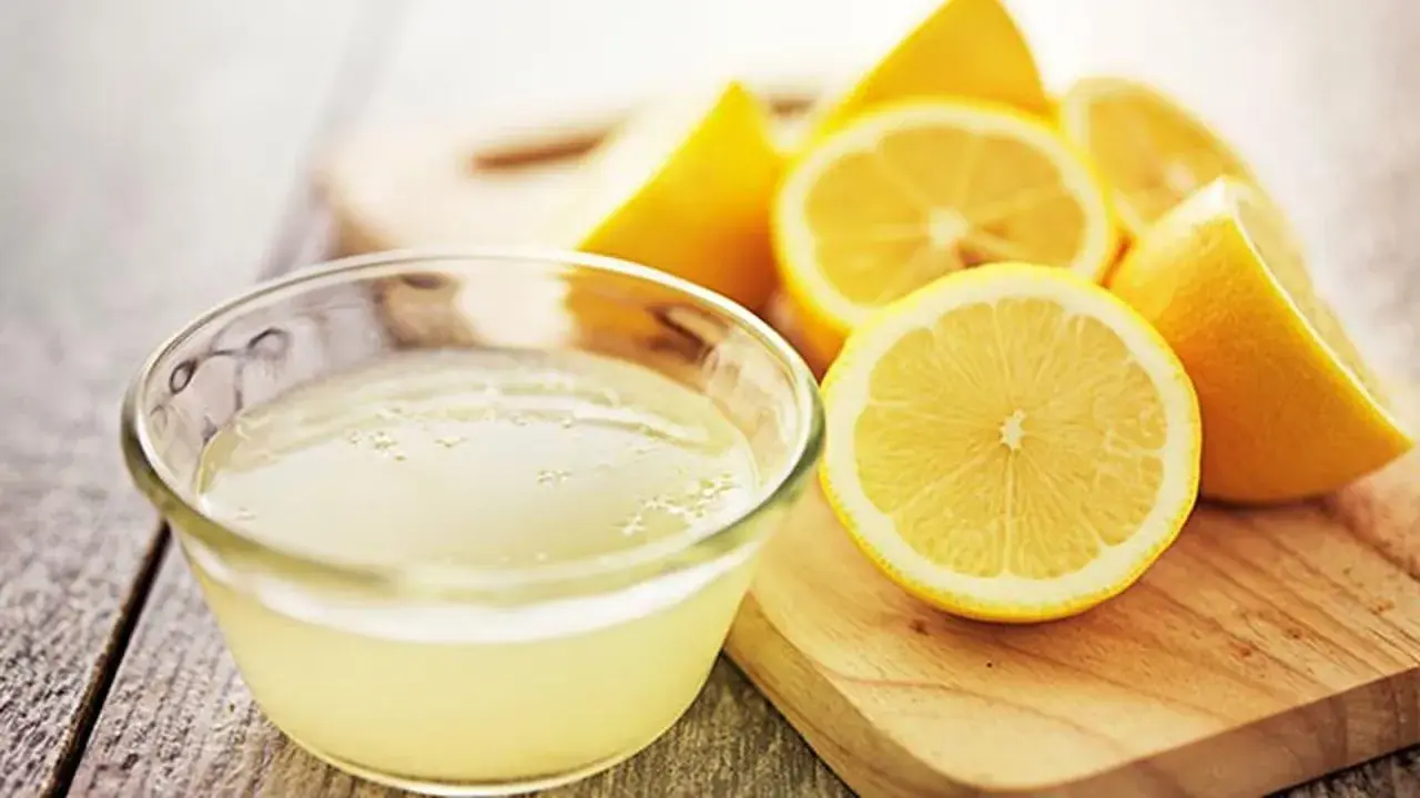 Un tazón de jugo de limón fresco y limones cortados, ideales como remedios caseros para el pelo graso.