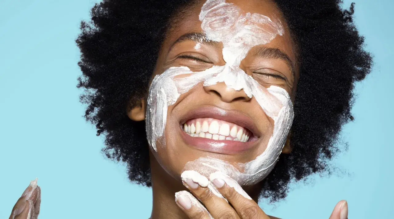 Una mujer sonríe con una mascarilla blanca en la cara. ¿Qué va primero el exfoliante o el limpiador?