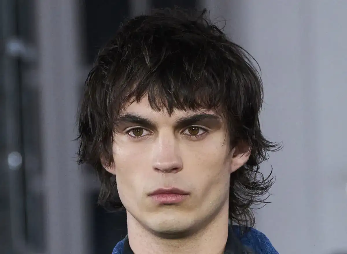 Hombre joven con un moderno mullet corto, cabello oscuro y despeinado, mirada intensa.