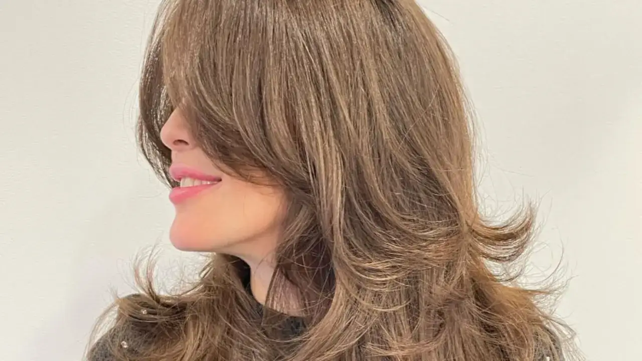 Mujer sonr&iacute;e con un corte mariposa en su cabello casta&ntilde;o, con capas que enmarcan su rostro.