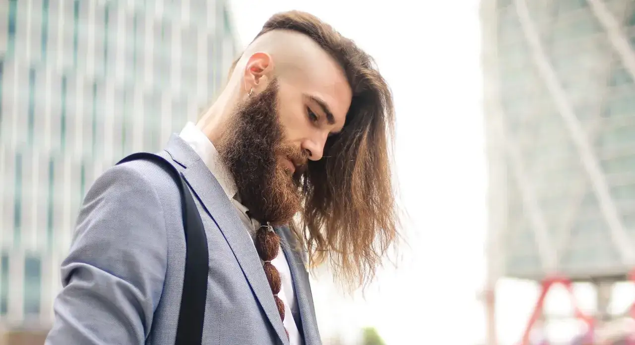 Hombre con pelo largo y barba, luciendo un traje azul claro. Su cabello largo cae sobre su hombro.