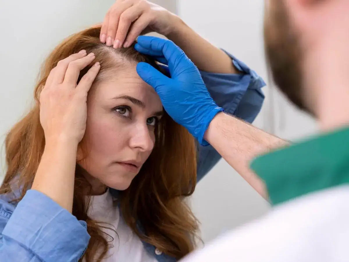 Mujer preocupada por su cabello fino y escaso, mientras un profesional evalúa su cuero cabelludo para un posible tratamiento.