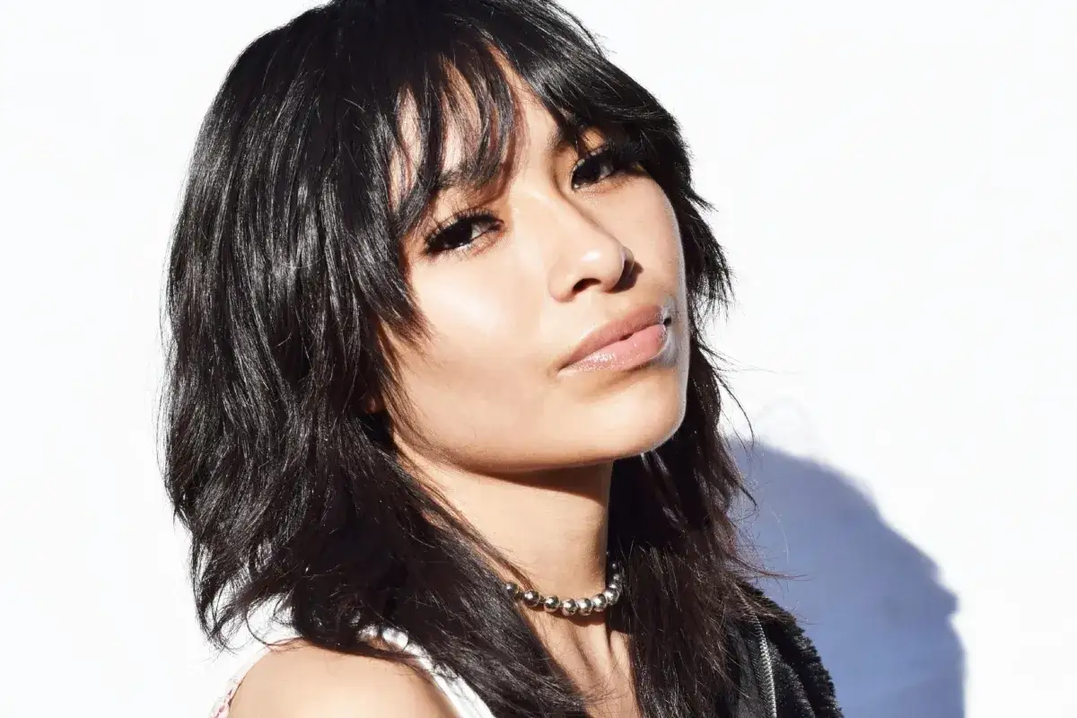 Mujer con un moderno corte de pelo mullet, labios brillantes y un collar plateado.