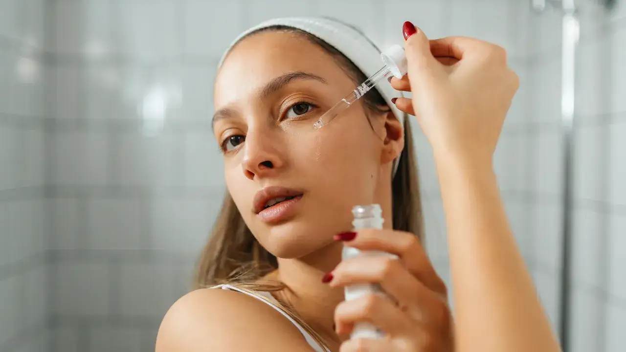 Mujer aplica aceite de ricino para la cara con un gotero. Su piel luce hidratada y radiante.