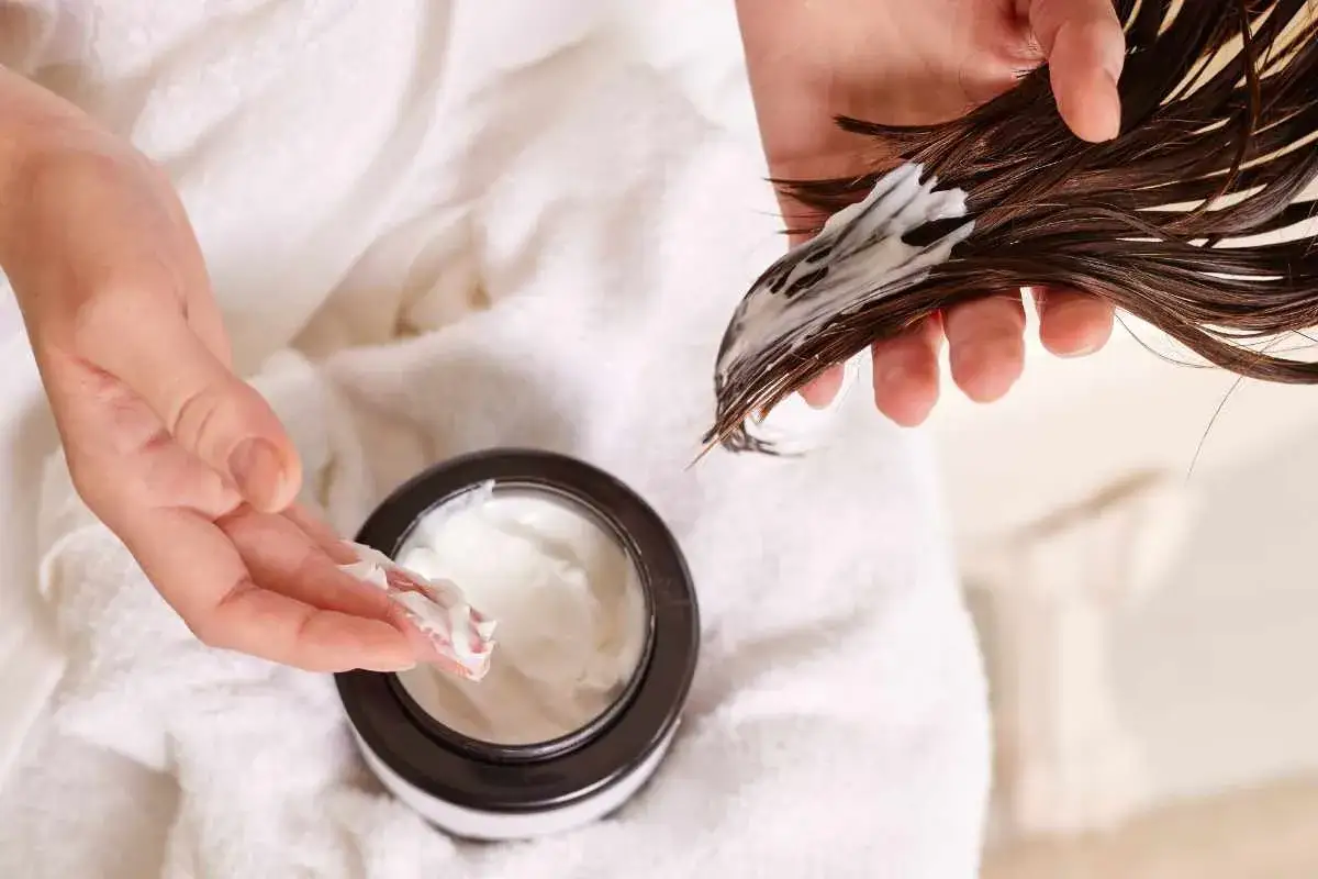 Manos aplicando Olaplex 3 como usar en cabello mojado. Crema blanca en la mano y mechón de pelo.
