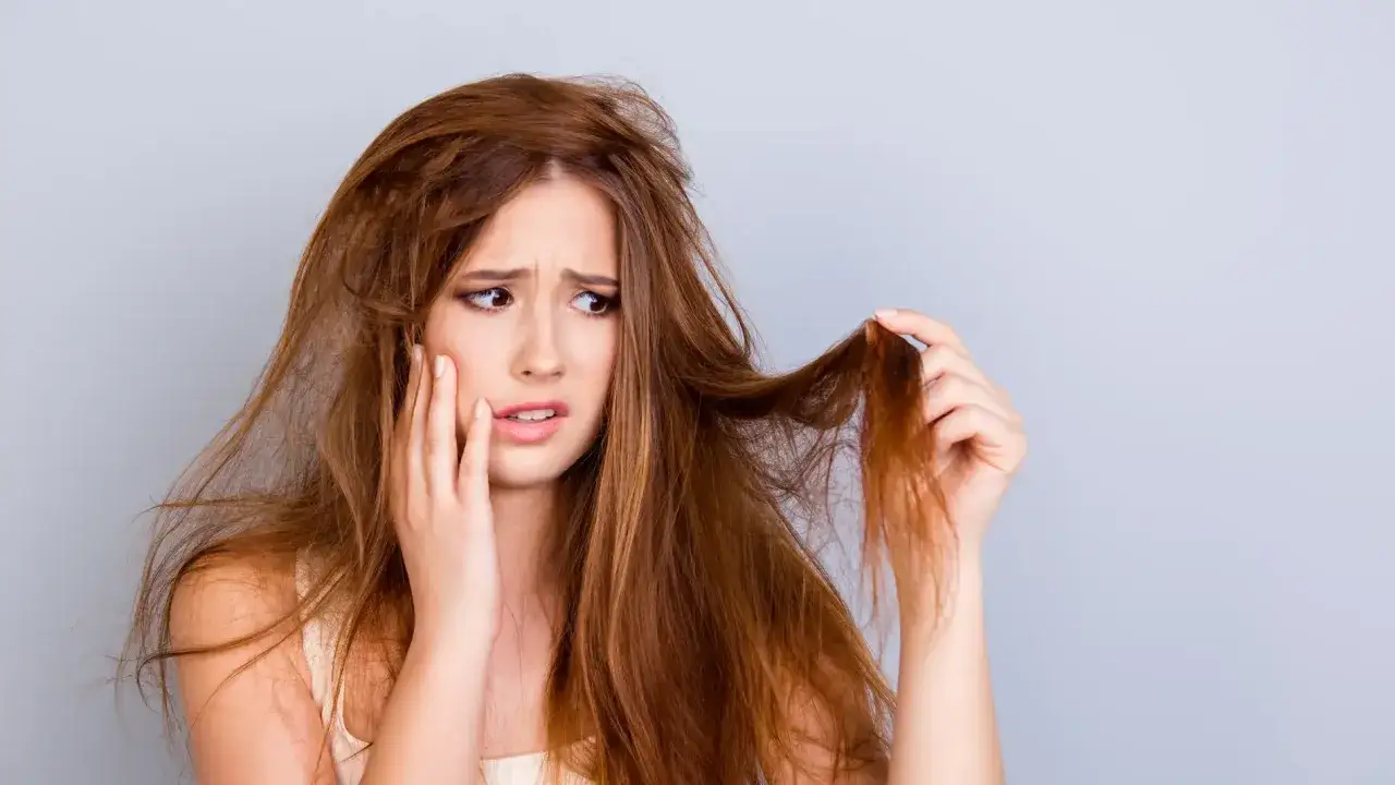 Mujer preocupada por su cabello apelmazado y da&ntilde;ado, que parece sin vida y enredado.