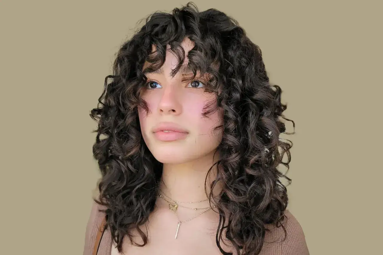 Chica con un moderno corte de pelo rizado a capas, con flequillo suelto y ondas definidas.